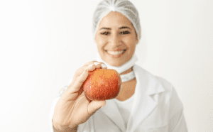 Nutricionista segurando uma maçã e vestida com jaleco e touca. 