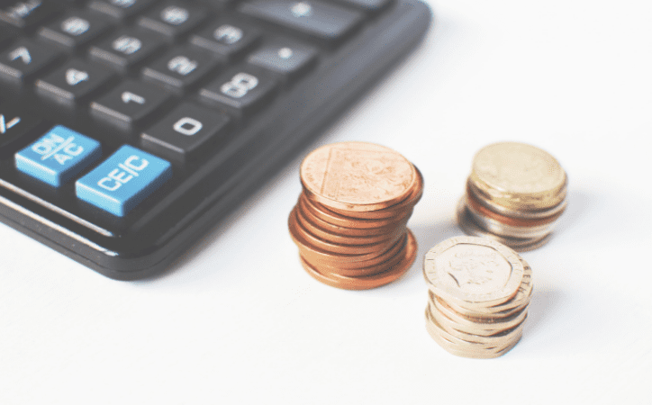 imagem de uma calculadora preta e ao lado três pequenas pilhas de moedas
