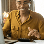 Mulher com camisa amarela mexendo no computador e na calculadora
