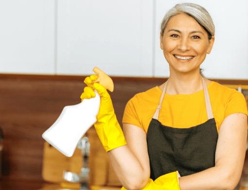 Mulher vestindo avental amarelo segurando um produto de limpeza.