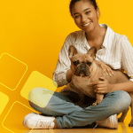 Mulher segurando um cachorro na frente de um fundo amarelo.