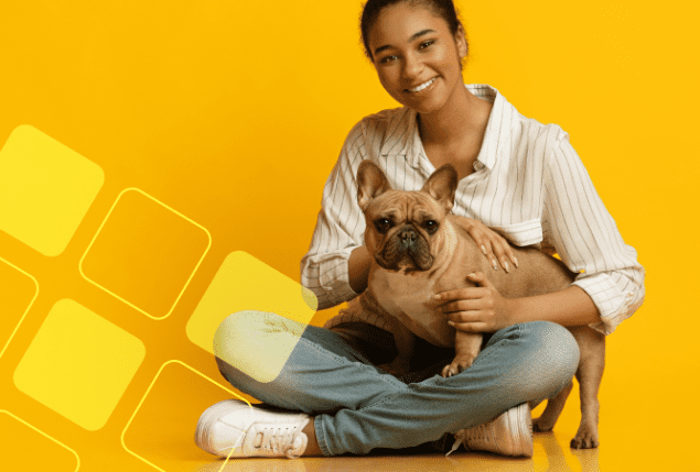 Mulher segurando um cachorro na frente de um fundo amarelo.