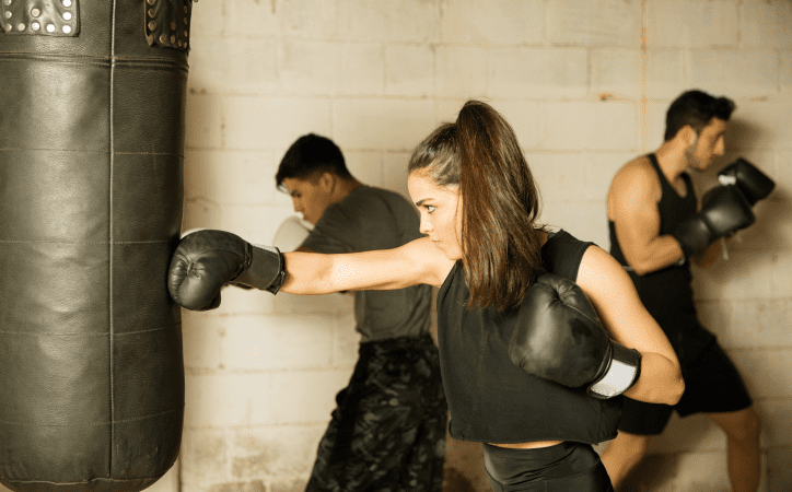 Homem e mulher vestidos de preto usando luvas de boxe e realizando movimentos do esporte.