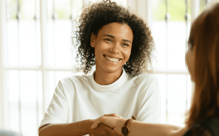 Mulher vestida de branco sorrindo e dando um aperto de mão com alguém.